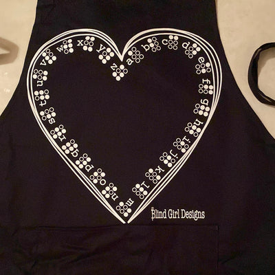 Black 37-inch heavy duty, cotton apron with long string ties and pull over the head strap. There are two big patch pockets on the front. Our highly tactile Braille heart print is featured on this apron. There is an outline of a hand drawn heart lined with the Braille alphabet inside. It kind of looks like lace!