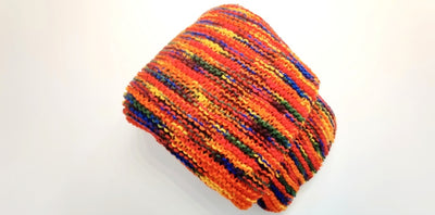 The blanket is primarily red with yellow, orange, green, and blue woven in. It is folded up on a table.