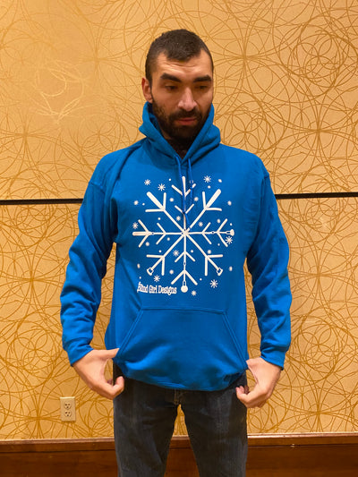 A tall male stands against a golden color wall wearing a royal blue colored hoodie. There is a large 12 by 12 chest print of a white 3D puff ink snowflake made of crossing 4 blind canes. They are crossed  like a spoke. Each spoke has 2V shapes, which gives it the snowflake outlook. There are tiny 3D snowflakes sprinkled around the main snowflake. It is a standard hoodie pullover sweatshirt fit with a large front pocket and large hood.