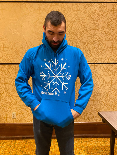 A tall male stands against a golden color wall wearing a royal blue colored hoodie. There is a large 12 by 12 chest print of a white 3D puff ink snowflake made of crossing 4 blind canes. They are crossed  like a spoke. Each spoke has 2V shapes, which gives it the snowflake outlook. There are tiny 3D snowflakes sprinkled around the main snowflake. It is a standard hoodie pullover sweatshirt fit with a large front pocket and large hood.