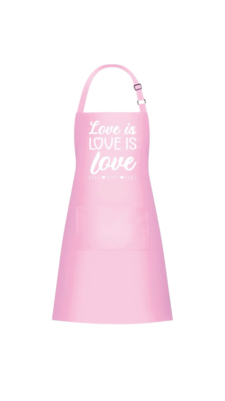 “Love is love is love” pink&nbsp;37-inch heavy duty cotton apron with long string ties and pull over the head strap. There are two big patch pockets on the front. The chest area has 3D puff print ink reading LOVE IS LOVE IS LOVE stacked one above the other in two beautiful fonts, complete with 3D tactile braille underneath the font.