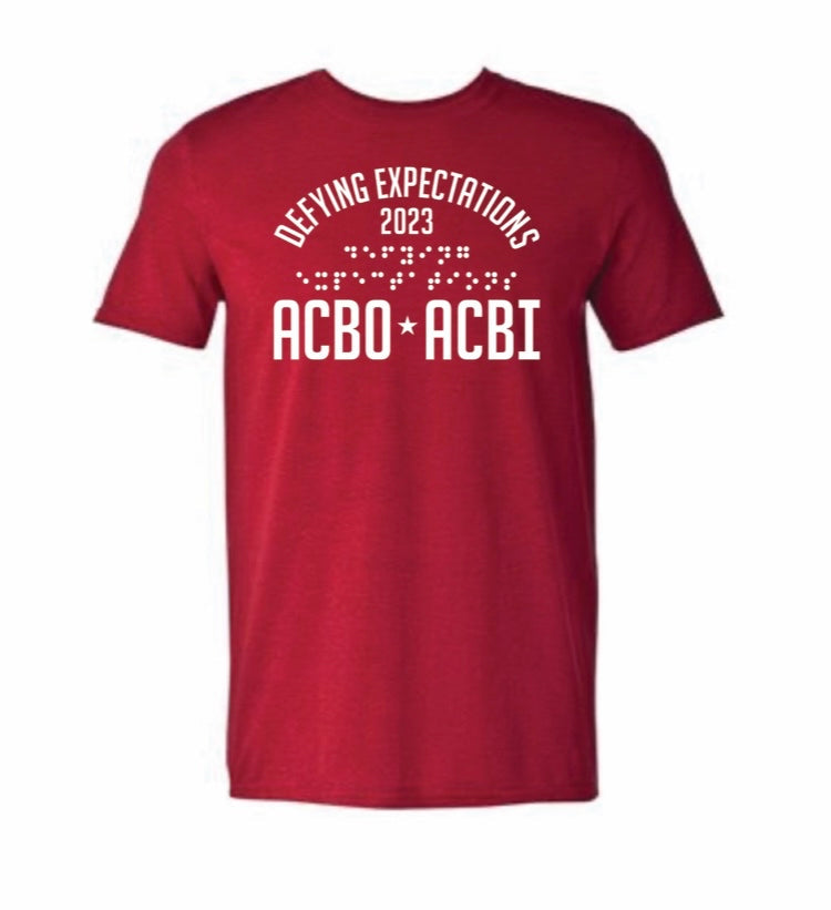 [Description: The t-shirt is a darker red color with a 9.75 x 12 inch rectangle print. The ink is white 3-D tactile puff Ink. In an arch across the entire print, says the words, proudly “Defying Expectations” Immediately below this arch of words is the date 2023. Across the entire print at the bottom are large capital  letters ACBO • ACBI]