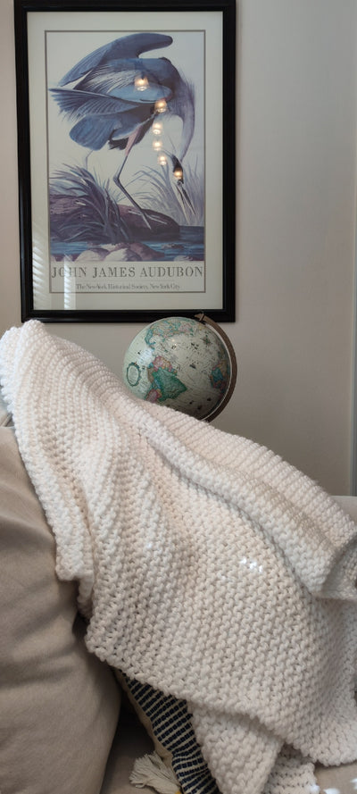 A large knit white blanket rests on a tan couch.