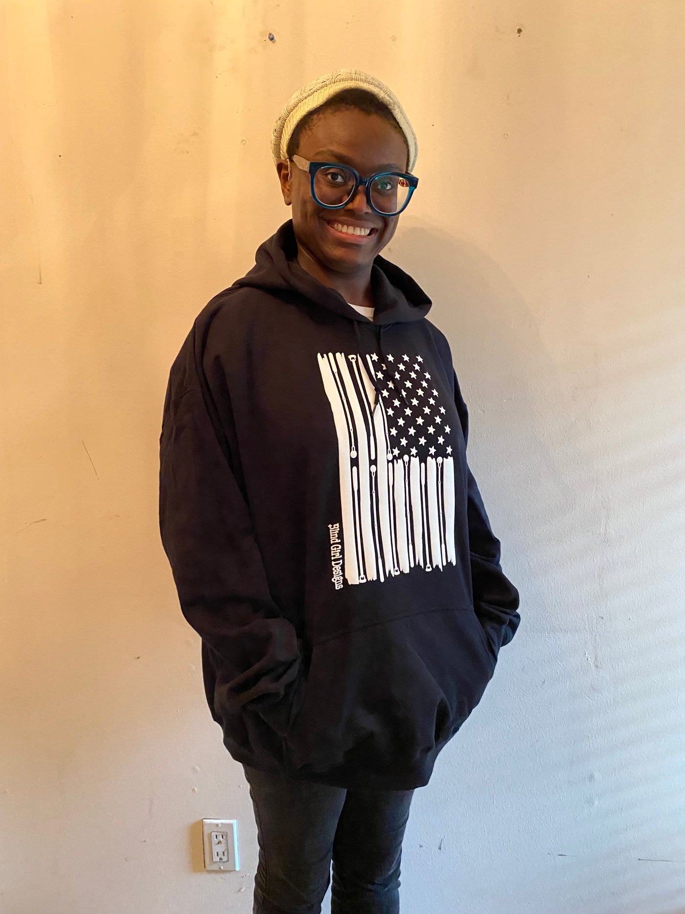 Cyndi is wearing a medium black hoodie, she is 5 foot 7 inches and medium is her normal size. It is a cool impression of the American flag. There are 50 stars and stripes that taper at the edges. The white stripes are made from a variety of white cane styles. The entire print is in tactile 3D puff print.