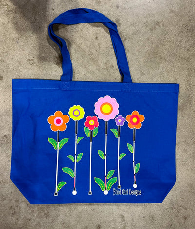 A blue canvas bag with five flowers with white canes as their stems decorate the front of the bag. The long handle is shown in its full arch. There are five flowers across the front of the bag with white canes as their stems. From left to right, the flowers are: Yellow with a pink and yellow middle, Coral with a yellow and light pink middle, Light pink with a dark pink and yellow middle, Lilac purple with a yellow middle, Orange with a dark pink and yellow middle.