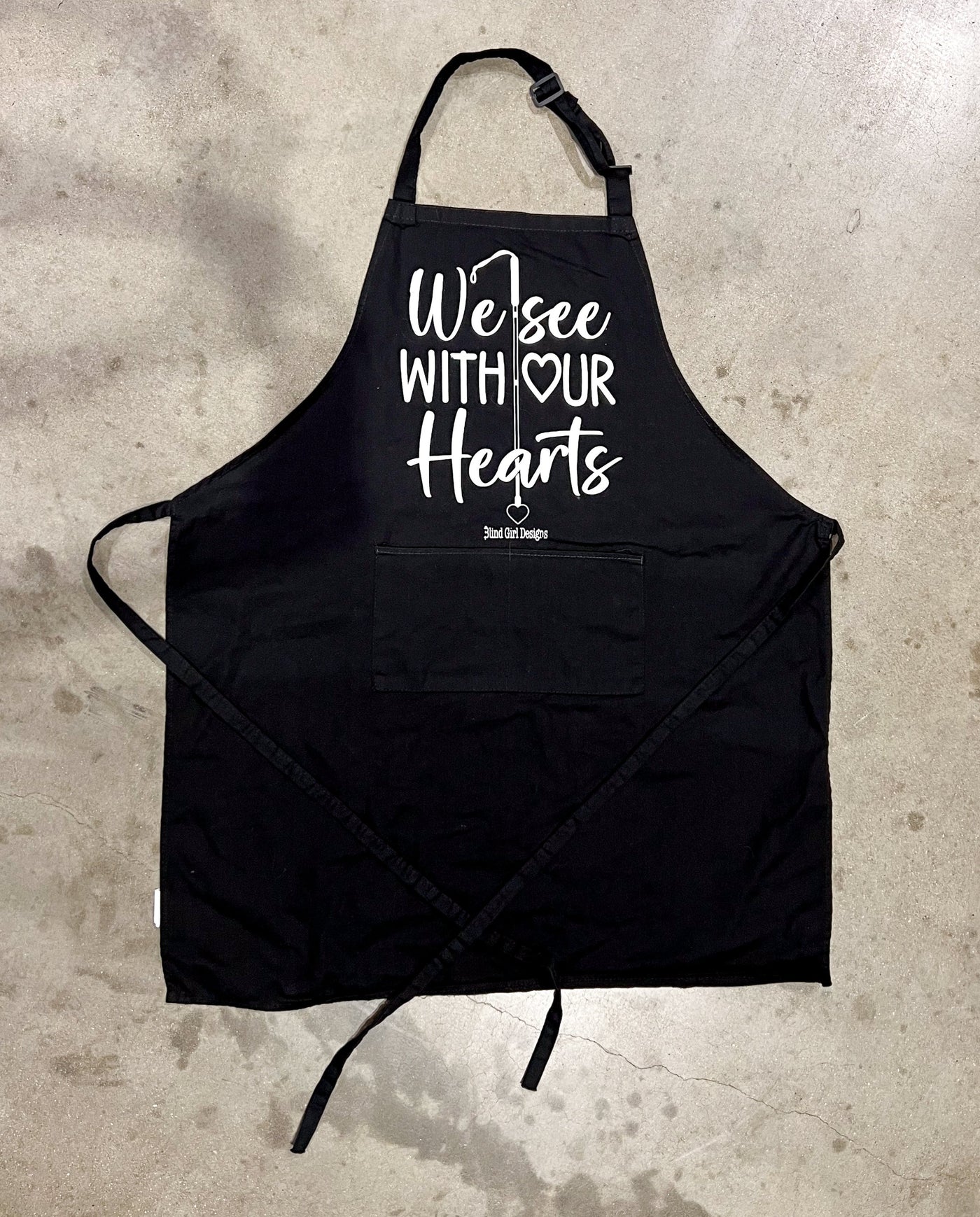 There is a big patch pockets on the front. This apron features our best selling "We See With Our Hearts" print on the front! There is a white cane running down the stack of words.