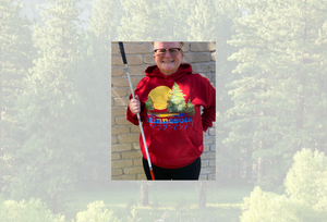 Tricia in a deep red hoodie with the Minnesota state ACB design. She is against a background of a pine tree forest.