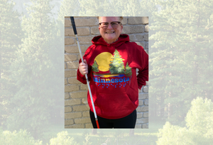Tricia in a deep red hoodie with the Minnesota state ACB design. She is against a background of a pine tree forest.