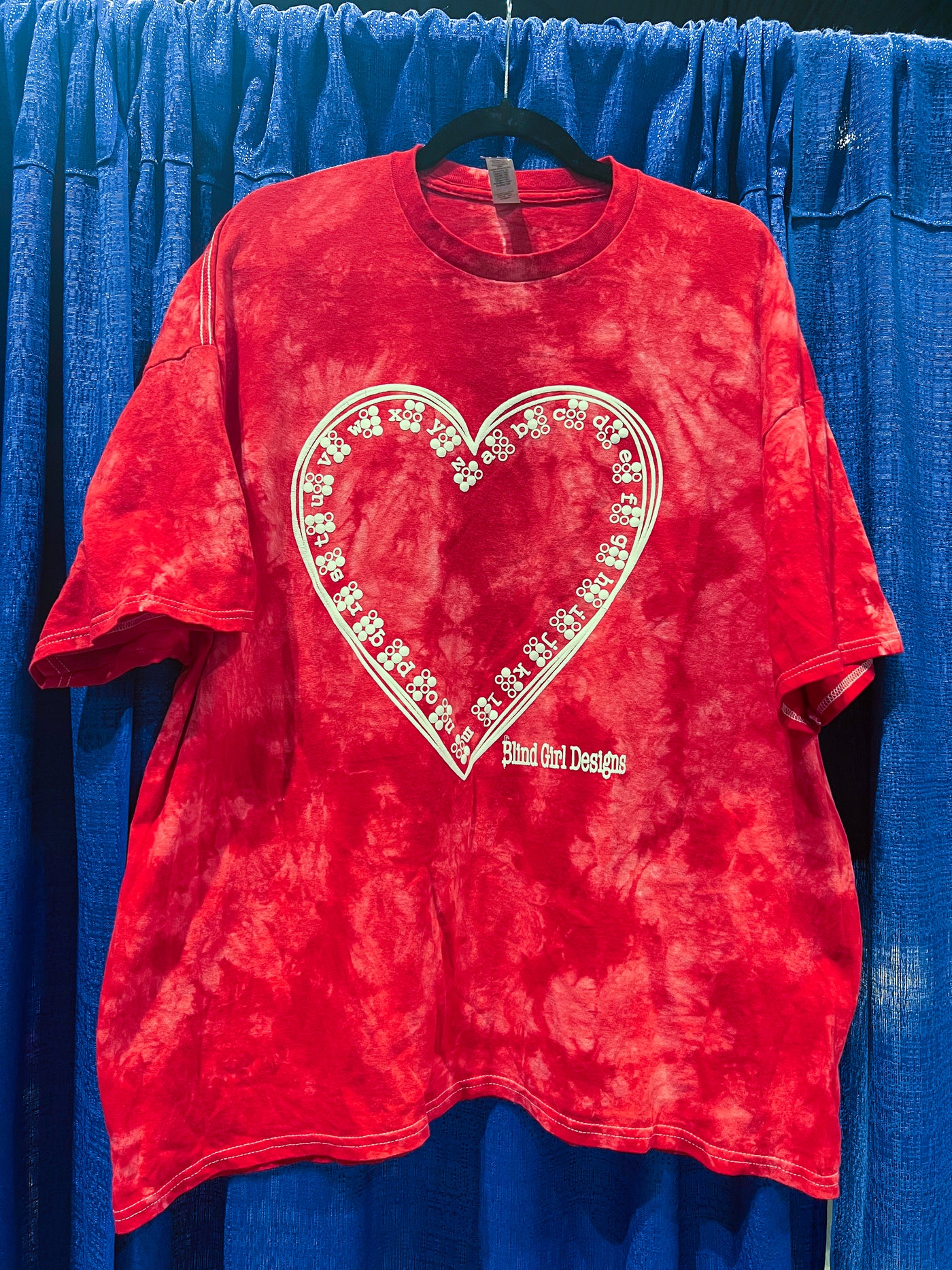 This dark and light red tie-dye shirt features the Braille ABCs lining the inside of a hand-drawn heart. It's printed in our puff ink so that it is tactile! It’s delightful.