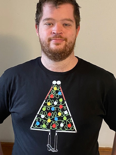 Robert is wearing a size 2 XL classic T-shirt which is his normal size. There is a large colorful chest print of a whimsical Christmas tree outlined by two blind canes, folded at the joints to make a triangle tree shape. The handles form the trunk and the roller balls form the outline of the top of the tree. The inside of the tree has green squiggles to suggest light strands with red, yellow, white, and blue ornaments shaped like a roller ball on the bottom of a cane.