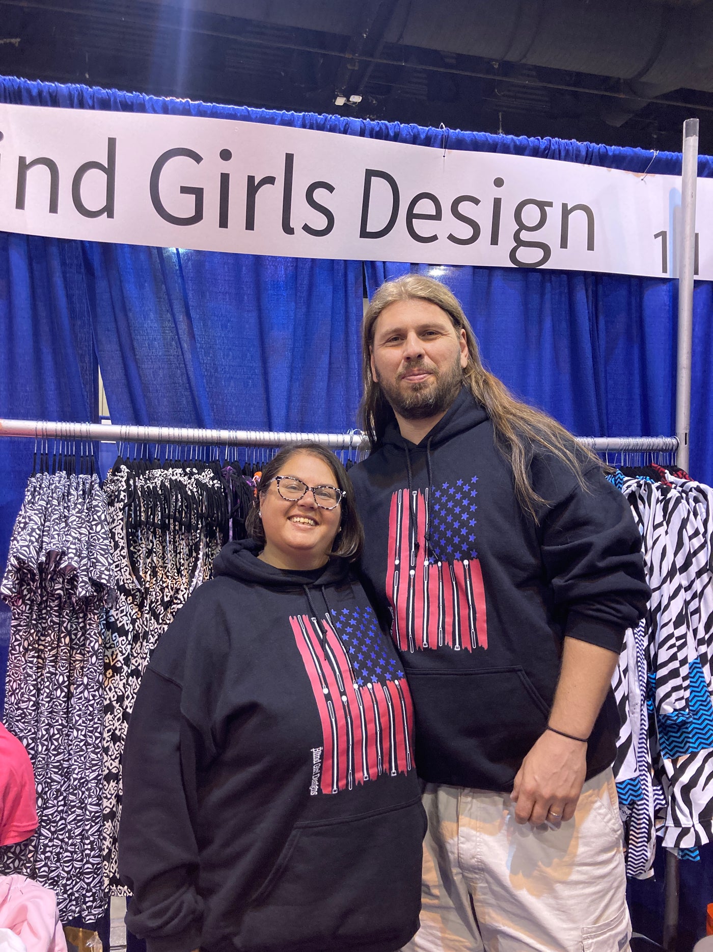 A short woman and tall man are wearing a medium black hoodie, she is 5 foot 7 inches and medium is her normal size. It is a cool impression of the American flag. There are 50 blue stars, and red stripes that taper at the edges. The white stripes are made from a variety of white cane styles.