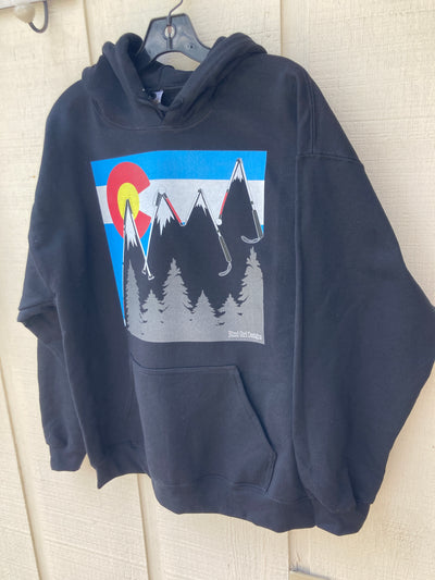 Black unisex hoodie with drawstrings. There is a large chest print of a big round yellow sun, which is surrounded by a red letter C. Across the entire print are light blue and yellow horizontal stripes. The stripes are interrupted by large blind canes which form the outline of the Rocky mountains in a zig zag pattern. Below the peaks of the mountains are white snow caps. At the bottom right of the print are a series of grey fir trees. The BLIND GIRL DESIGNS logo is in the lower right hand side of the trees.