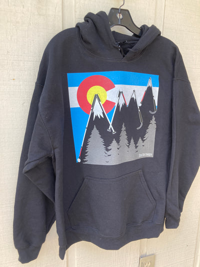 Black unisex hoodie with drawstrings. There is a large chest print of a big round yellow sun, which is surrounded by a red letter C. Across the entire print are light blue and yellow horizontal stripes. The stripes are interrupted by large blind canes which form the outline of the Rocky mountains in a zig zag pattern. Below the peaks of the mountains are white snow caps. At the bottom right of the print are a series of grey fir trees. The BLIND GIRL DESIGNS logo is in the lower right hand side of the trees.